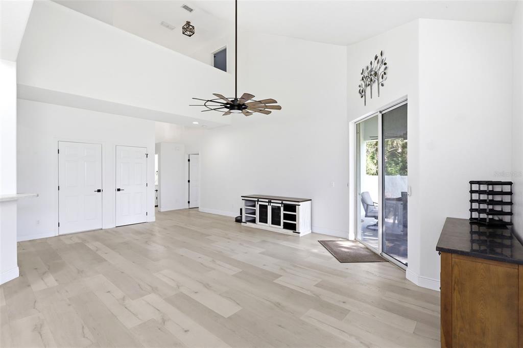 A bright living room features high ceilings, light wood-look flooring, and a sliding glass door — 609 RHODES DRIVE, DELAND, FL