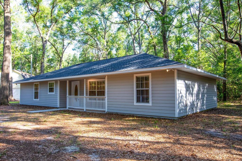 A single-story house with gray horizontal siding and a white porch sits among trees — 15713 NW 268TH TERRACE, HIGH SPRINGS, FL