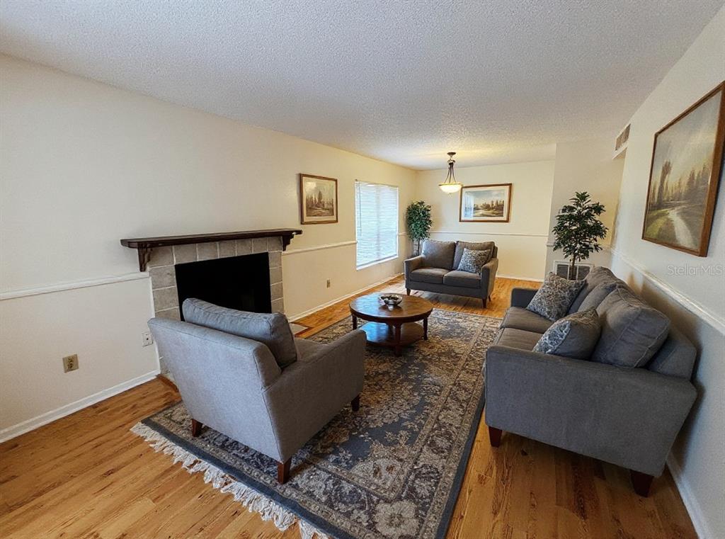 A living room features a stone fireplace, hardwood floors, and gray furniture on a rug — 4034 DREAM OAK PLACE UNIT 104, TAMPA, FL