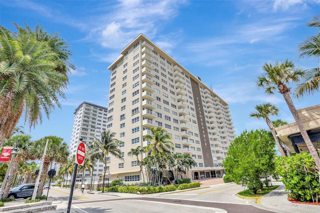 A multi-story residential building with balconies stands near palm trees and a street intersection — 133 N Pompano Beach Boulevard # 108, Pompano Beach FL 33062, POMPANO BEACH, FL
