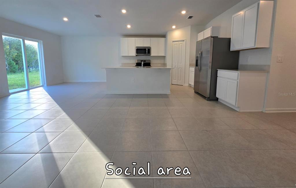An open-concept kitchen and living area features white cabinetry, stainless steel appliances, and tile flooring — 5034 BARNET DRIVE, DAVENPORT, FL