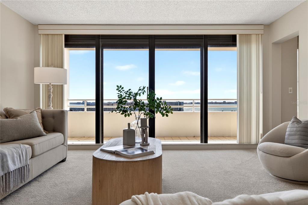 A living room features a beige sofa, a wooden coffee table, and floor-to-ceiling windows — 5950 PELICAN BAY PLAZA S UNIT 2E, GULFPORT, FL