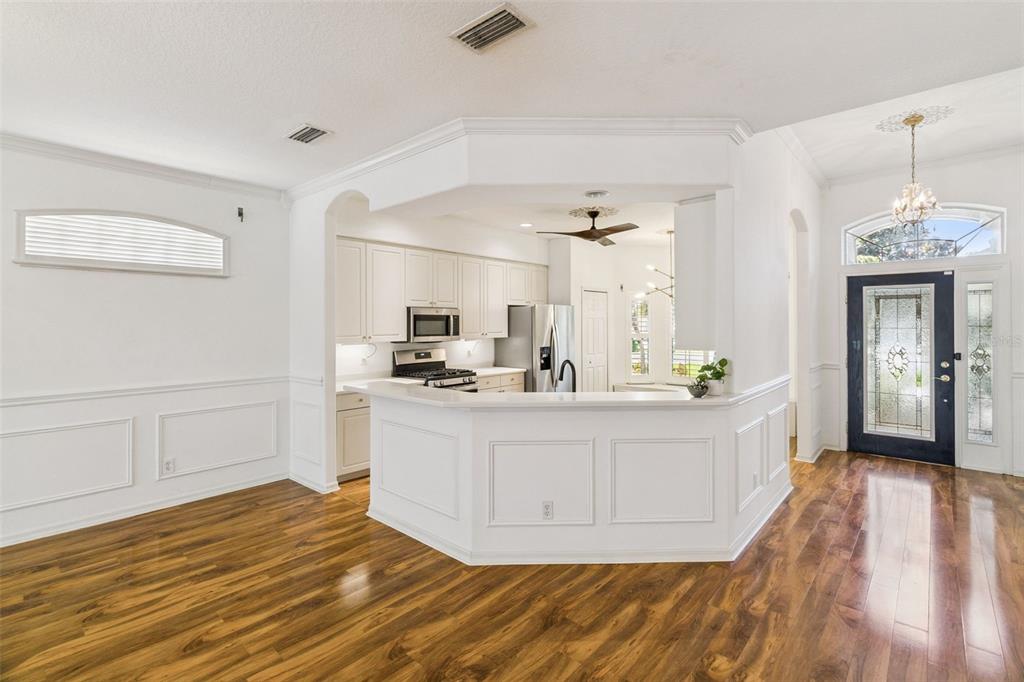 A kitchen with white cabinets and a breakfast bar overlooks a dining area with wood floors — 4680 PORTAGE TRAIL, MELBOURNE, FL