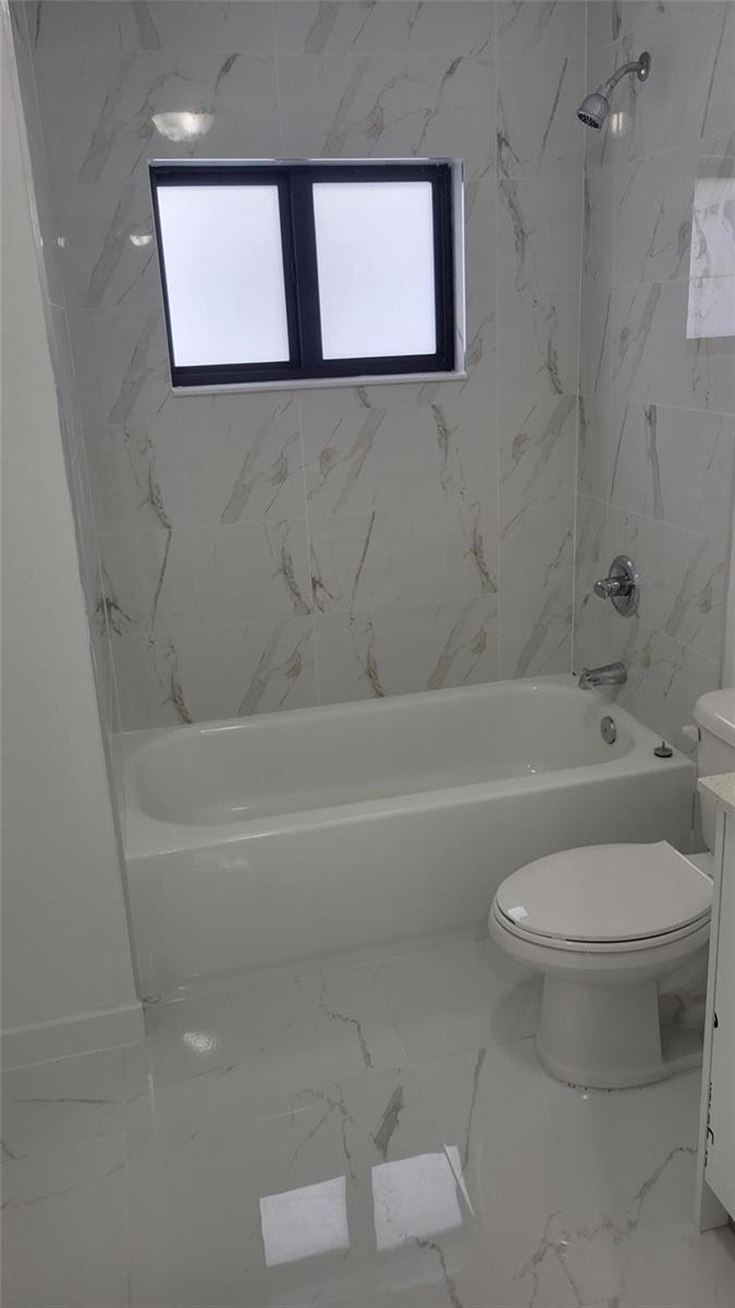 A bathroom features a white bathtub, a toilet, and white marble-patterned tile walls and floors — 1836 NW 70th Street, Miami FL 33147, MIAMI, FL