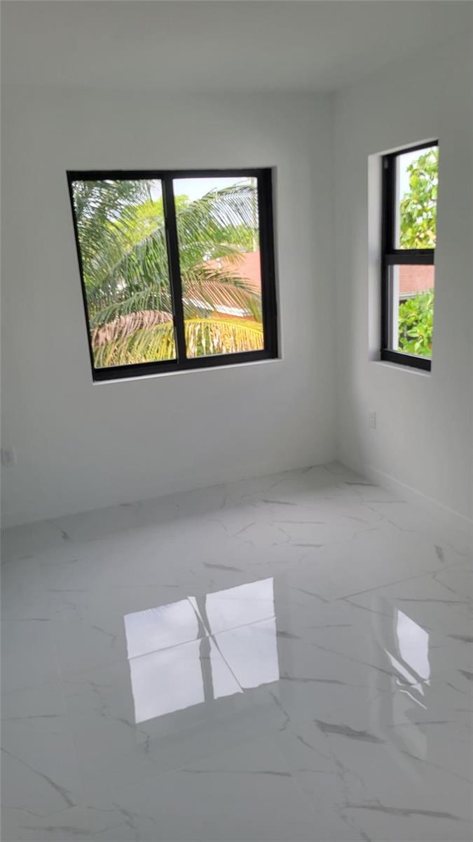 An empty room with white walls, glossy marble-look tile flooring, and black-framed windows — 1836 NW 70th Street, Miami FL 33147, MIAMI, FL