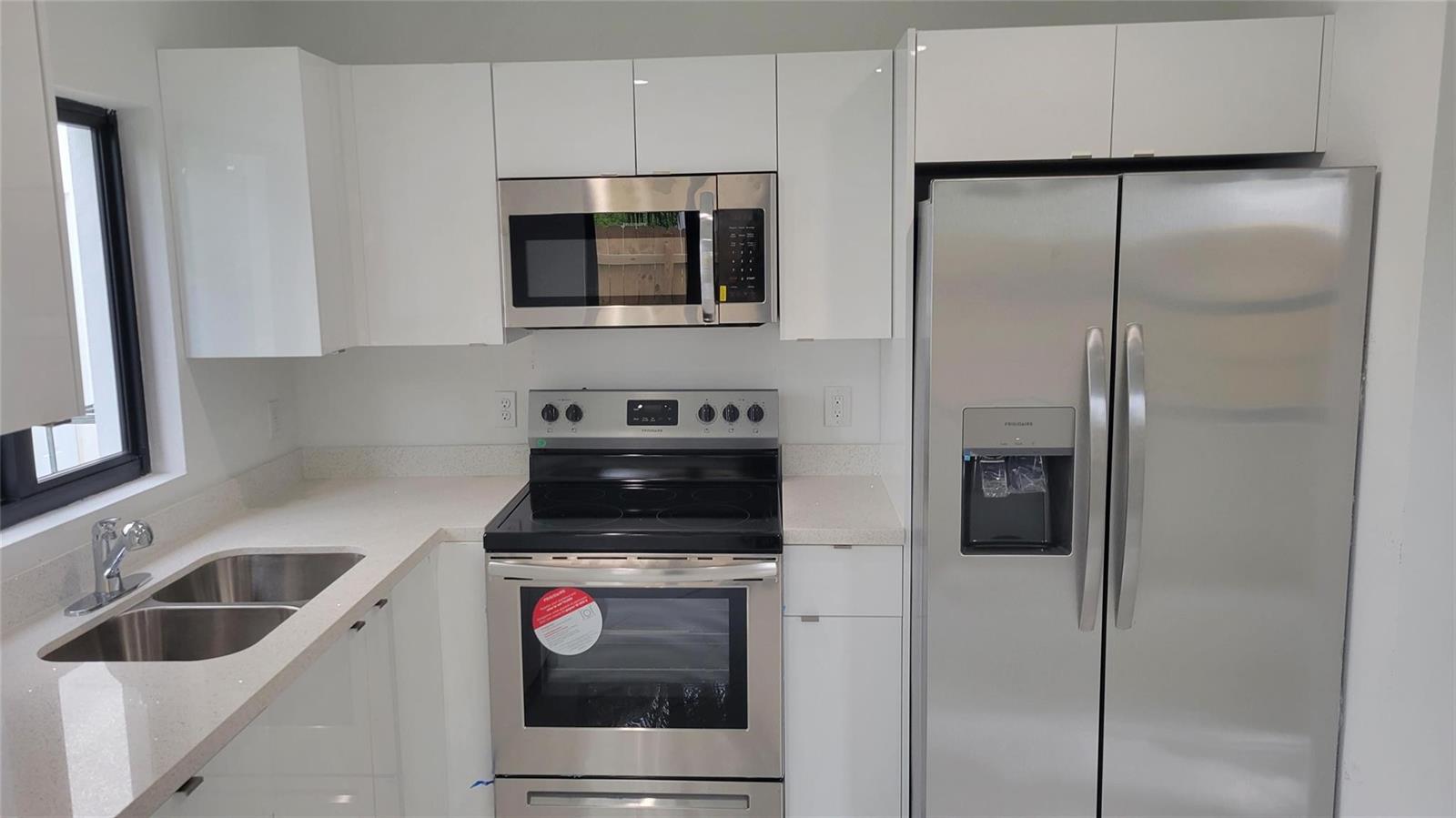 A kitchen features white cabinets, stainless steel appliances, and light-colored countertops — 1836 NW 70th Street, Miami FL 33147, MIAMI, FL