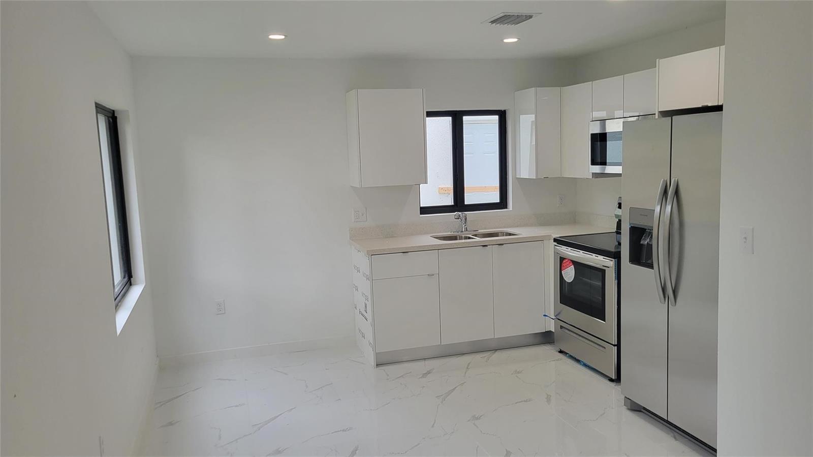 A modern kitchen features white cabinets, stainless steel appliances, and white marble-patterned tile flooring — 1836 NW 70th Street, Miami FL 33147, MIAMI, FL