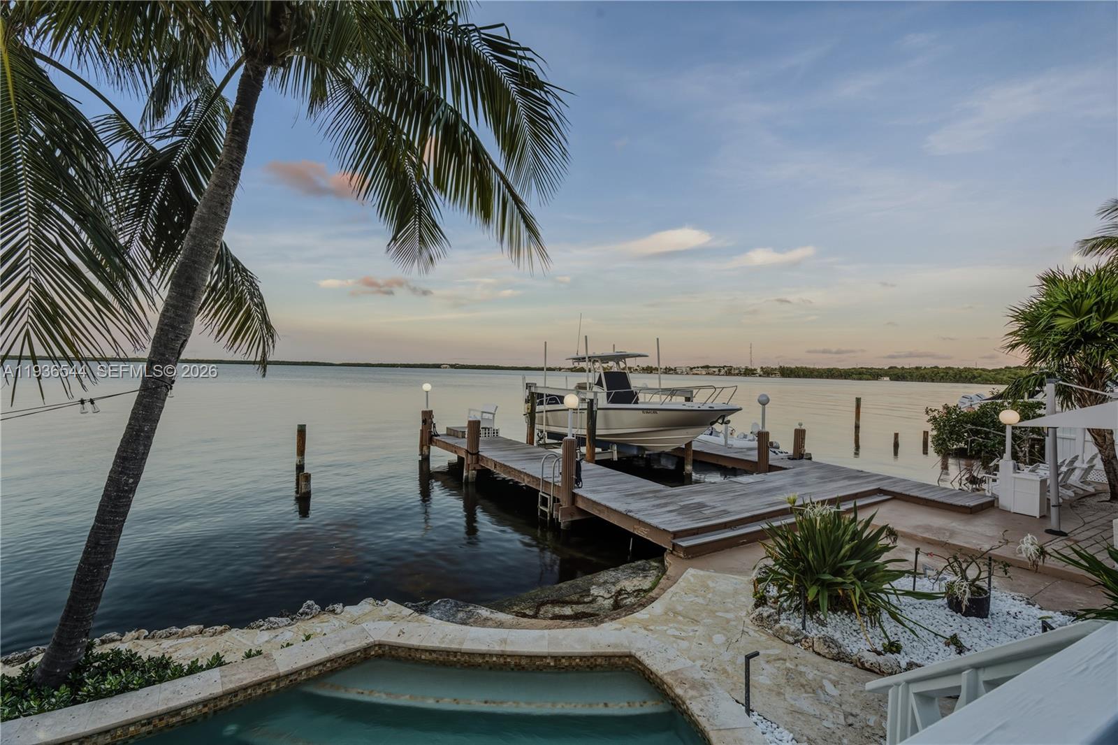 A boat sits on a lift at a wooden dock next to a waterfront pool — 16 North Dr, Key Largo FL 33037, KEY LARGO, FL