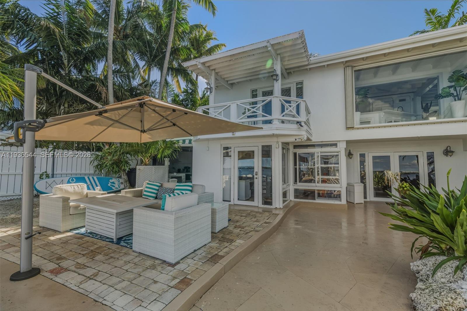 A white two-story house features a paved patio with outdoor furniture and a large umbrella — 16 North Dr, Key Largo FL 33037, KEY LARGO, FL