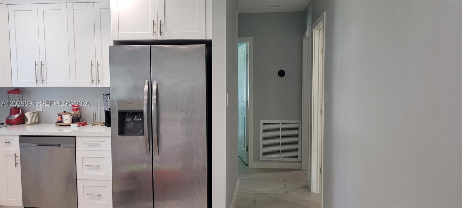 A tufted grey sofa sits in a living area adjacent to an open-concept white kitchen — 701 NE 14th St, Homestead FL 33030, HOMESTEAD, FL