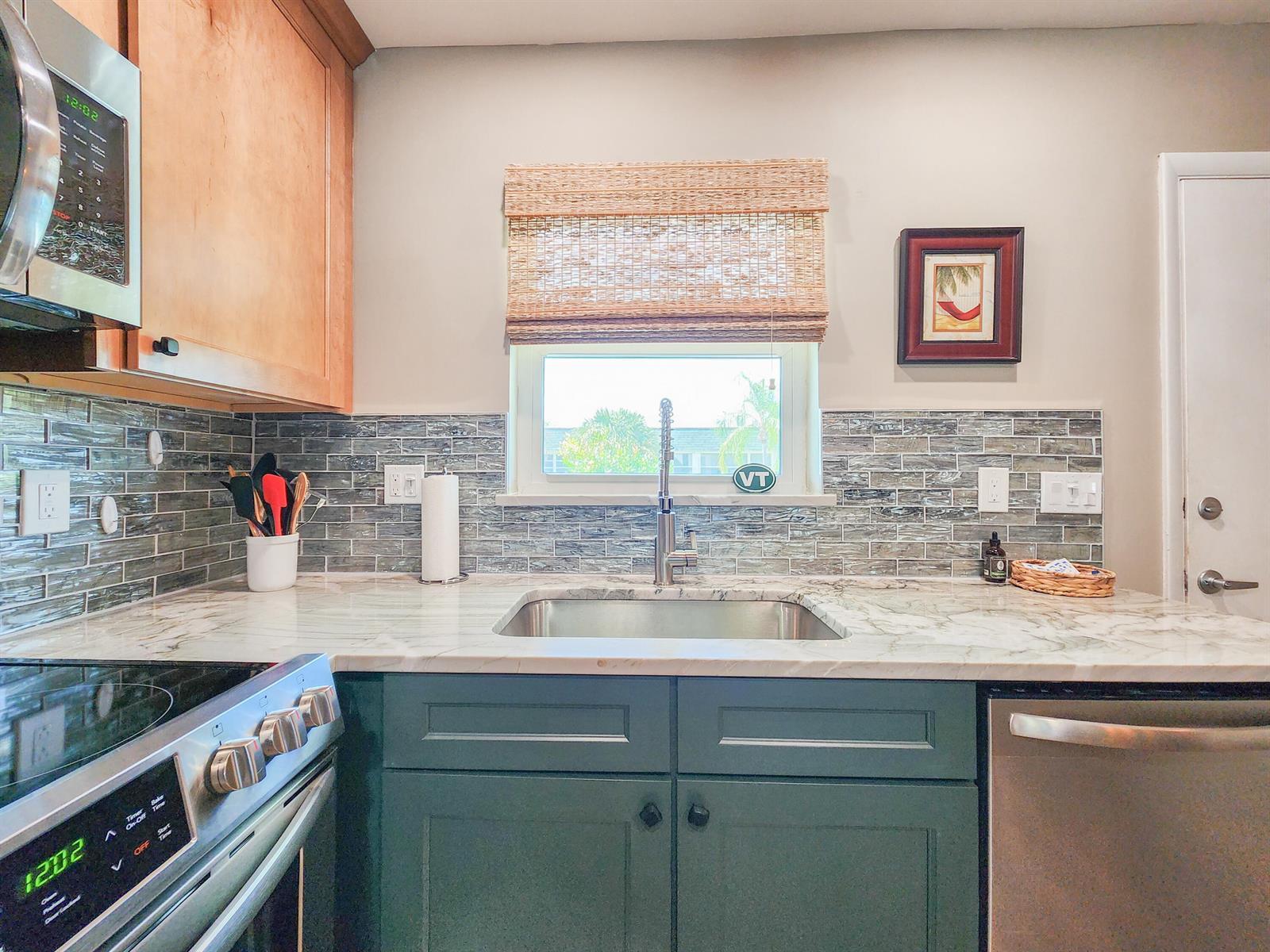 A kitchen features green cabinets, marble countertops, a tiled backsplash, and a stainless steel sink — 2800 Indian River Boulevard # 8, Vero Beach FL 32960, VERO BEACH, FL