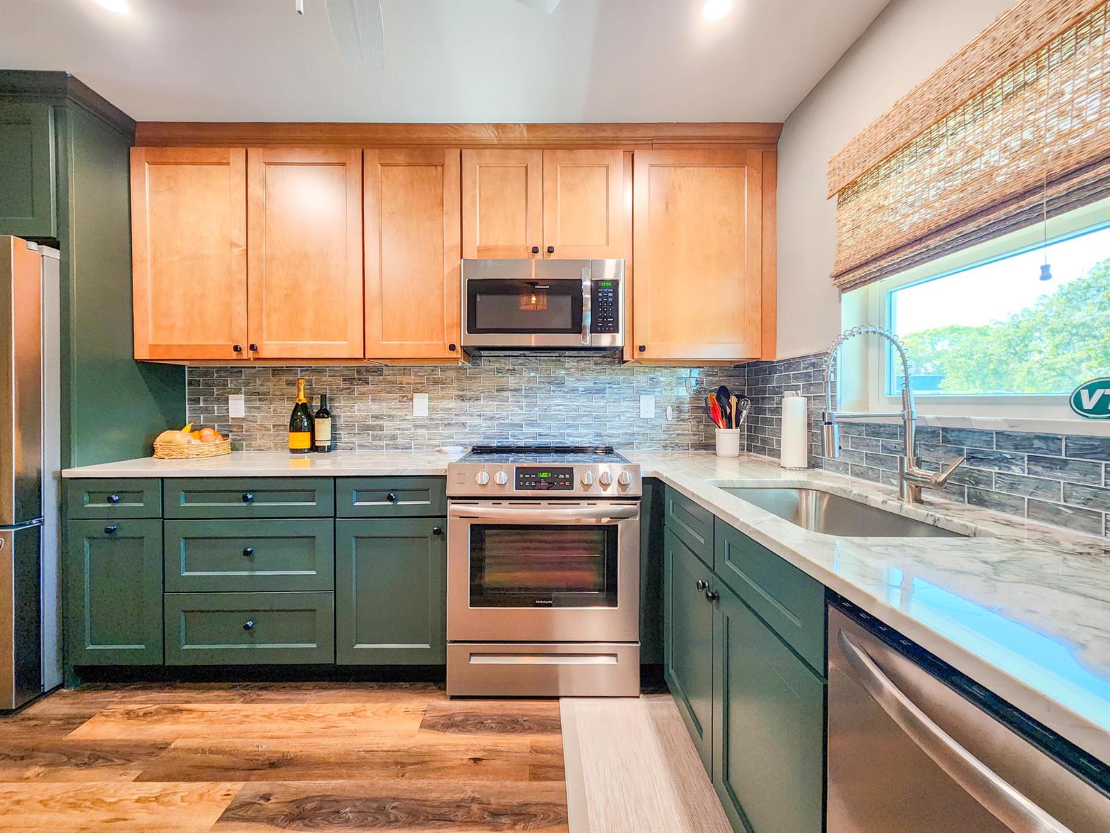 A kitchen features green lower cabinets, natural wood upper cabinets, stainless steel appliances, and tile backsplash — 2800 Indian River Boulevard # 8, Vero Beach FL 32960, VERO BEACH, FL