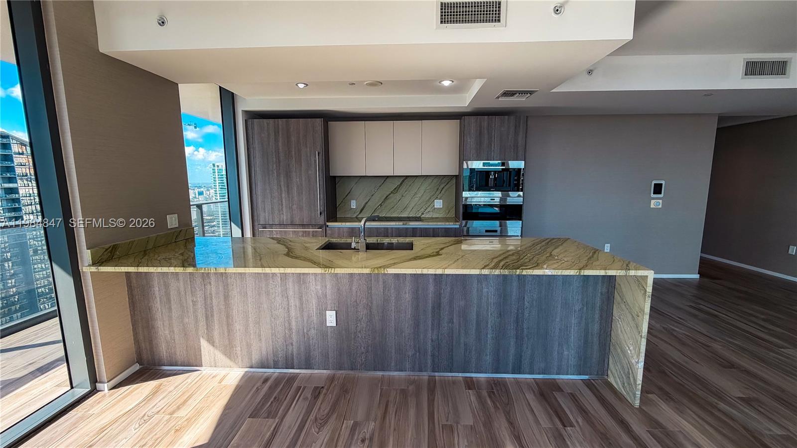 A modern kitchen features a large stone island, wood cabinetry, and floor-to-ceiling windows — 801 S Miami Ave # 4501, Miami FL 33130, MIAMI, FL