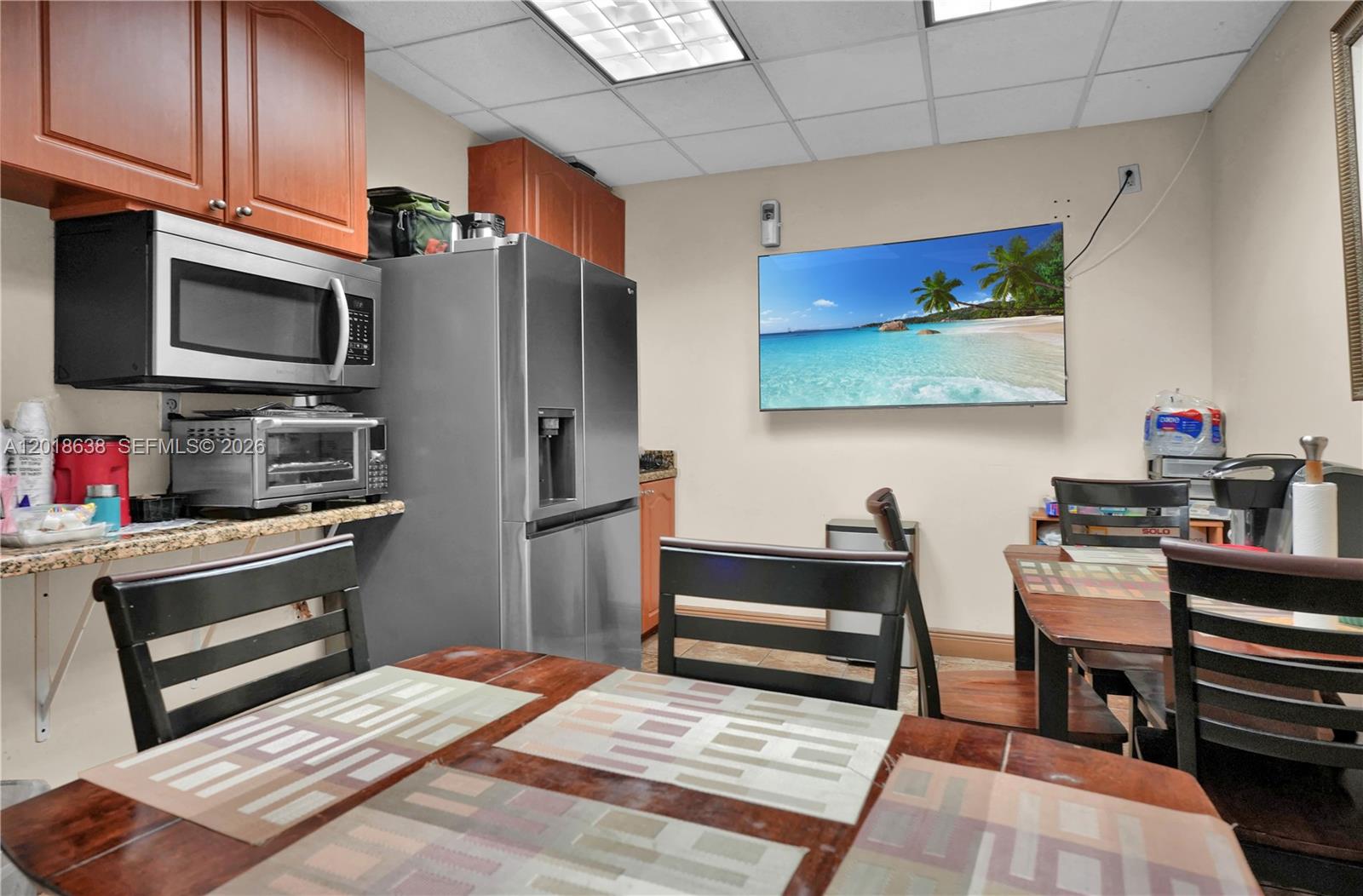 A kitchen features wooden cabinets, stainless steel appliances, a wall-mounted television, and dining tables — 12601 NW 115th Ave # 114, Medley FL 33178, MEDLEY, FL