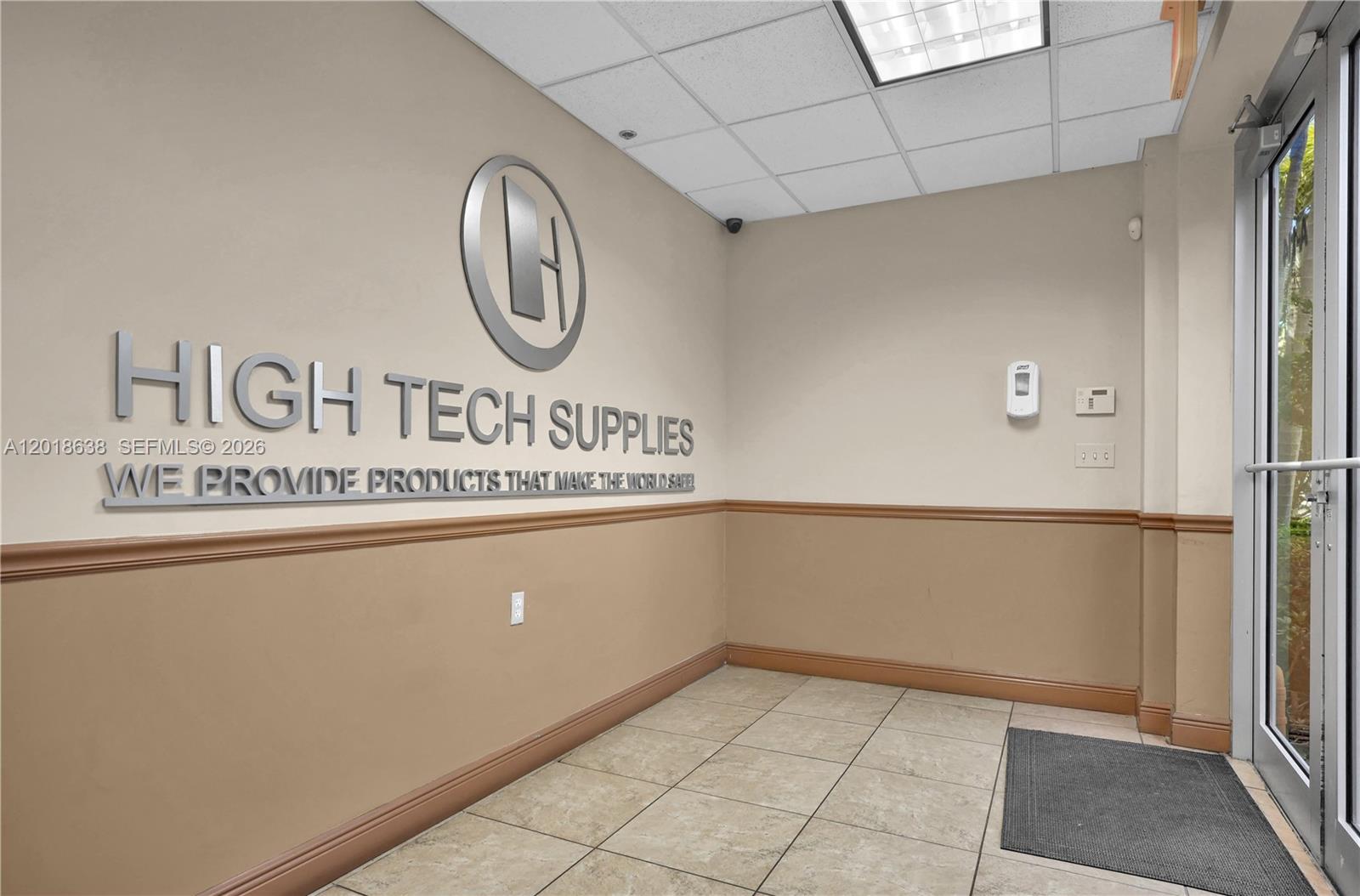 An office entrance features a logo on the wall, tile flooring, and a glass door — 12601 NW 115th Ave # 114, Medley FL 33178, MEDLEY, FL