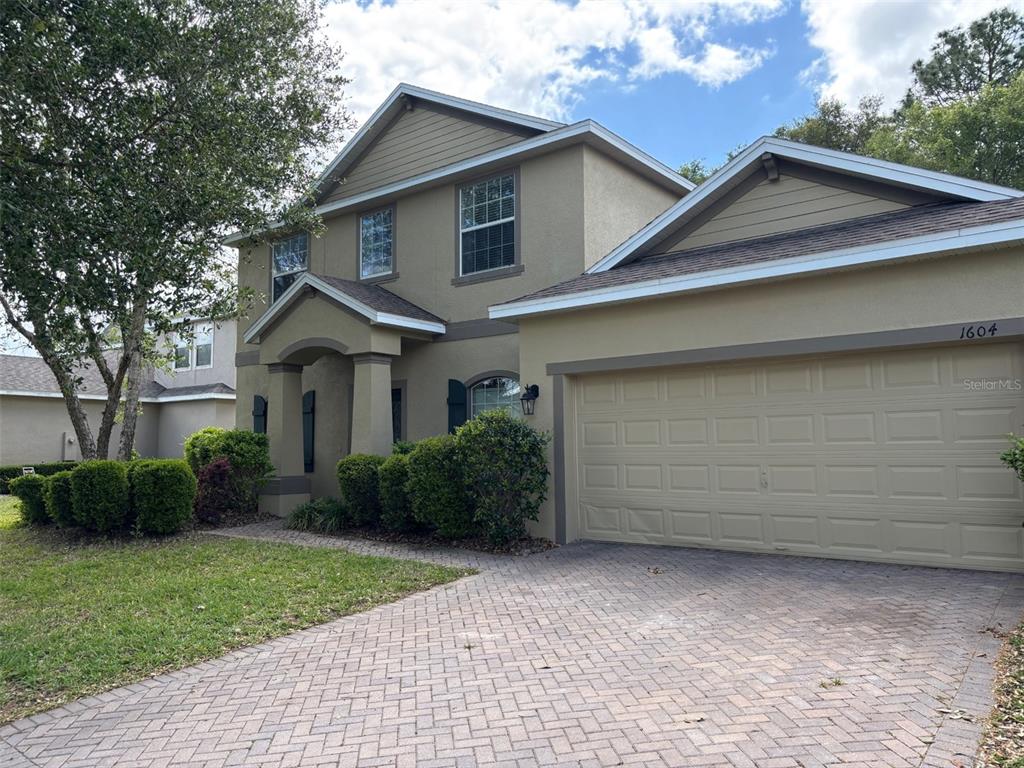 A two-story house with a tan stucco exterior, a brick paver driveway, and a garage — 1604 BLUE GRASS BOULEVARD, DELAND, FL