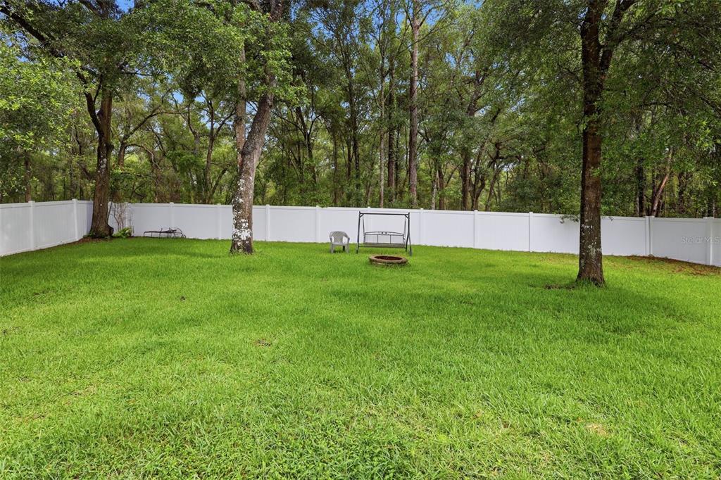A grassy backyard features a white vinyl fence, mature trees, and a metal swing set — 1604 BLUE GRASS BOULEVARD, DELAND, FL