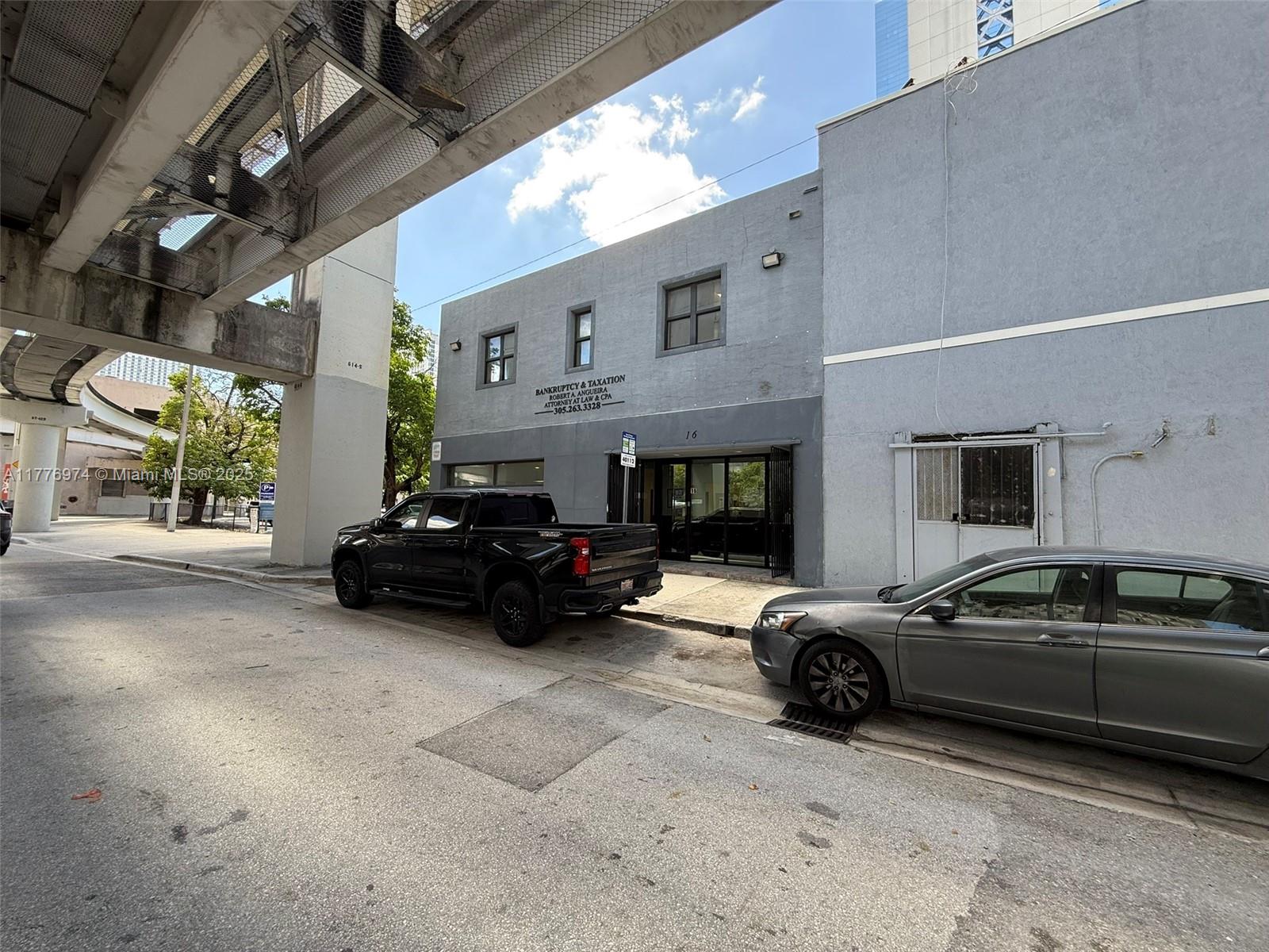 A gray two-story commercial building sits beneath an elevated train track with parked vehicles outside — 16 SW 1st Ave, Miami FL 33130, MIAMI, FL