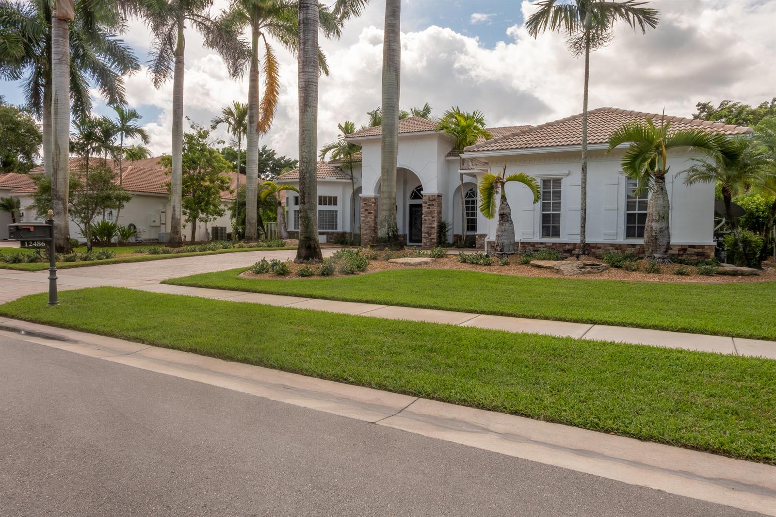 A white single-story house with a tile roof, stone accents, and palm trees in front — 12486 Equine Lane, Wellington FL 33414, WELLINGTON, FL