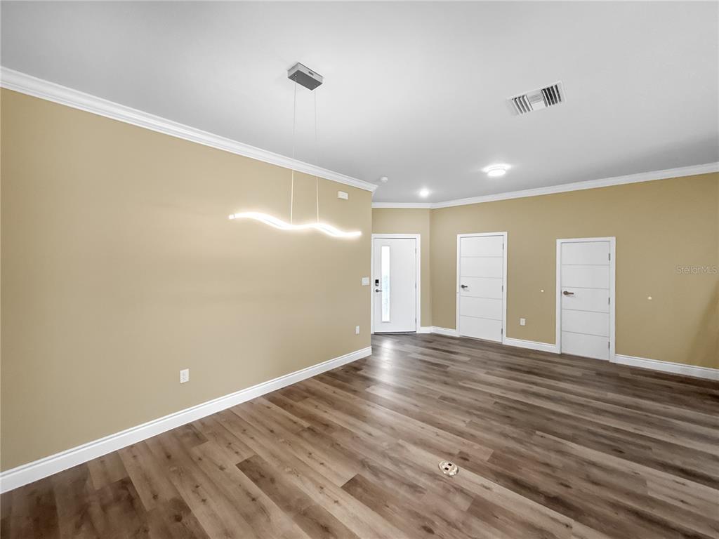 An empty room features light tan walls, wood-look flooring, a modern light fixture, and three doors — 1839 BRENTWOOD COURT, DAVENPORT, FL