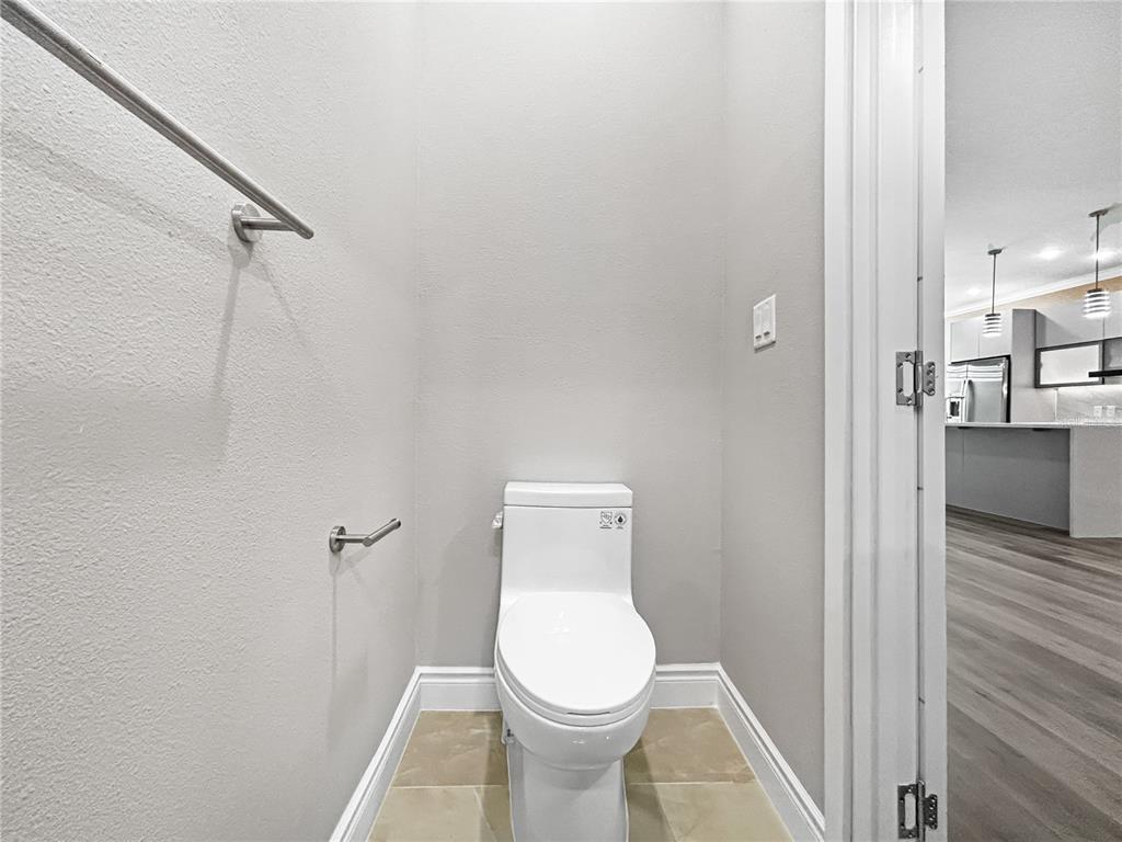 A small bathroom features a white toilet, light-colored tile flooring, and a wall-mounted grab bar — 1839 BRENTWOOD COURT, DAVENPORT, FL