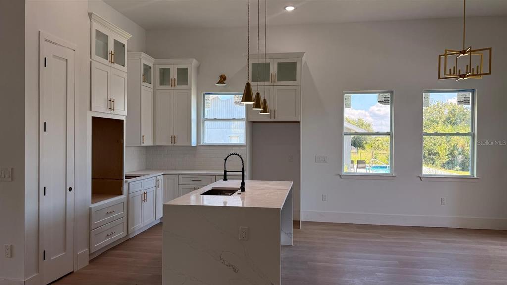 A modern kitchen features white cabinetry, a marble-topped island, and windows overlooking a backyard pool — 9500 GALAXIE CIRCLE, PORT CHARLOTTE, FL