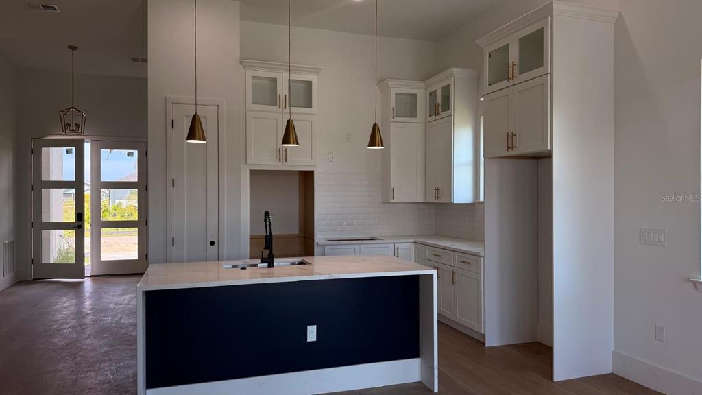 A kitchen features white cabinetry, a dark-paneled island with a sink, and three pendant lights — 9500 GALAXIE CIRCLE, PORT CHARLOTTE, FL