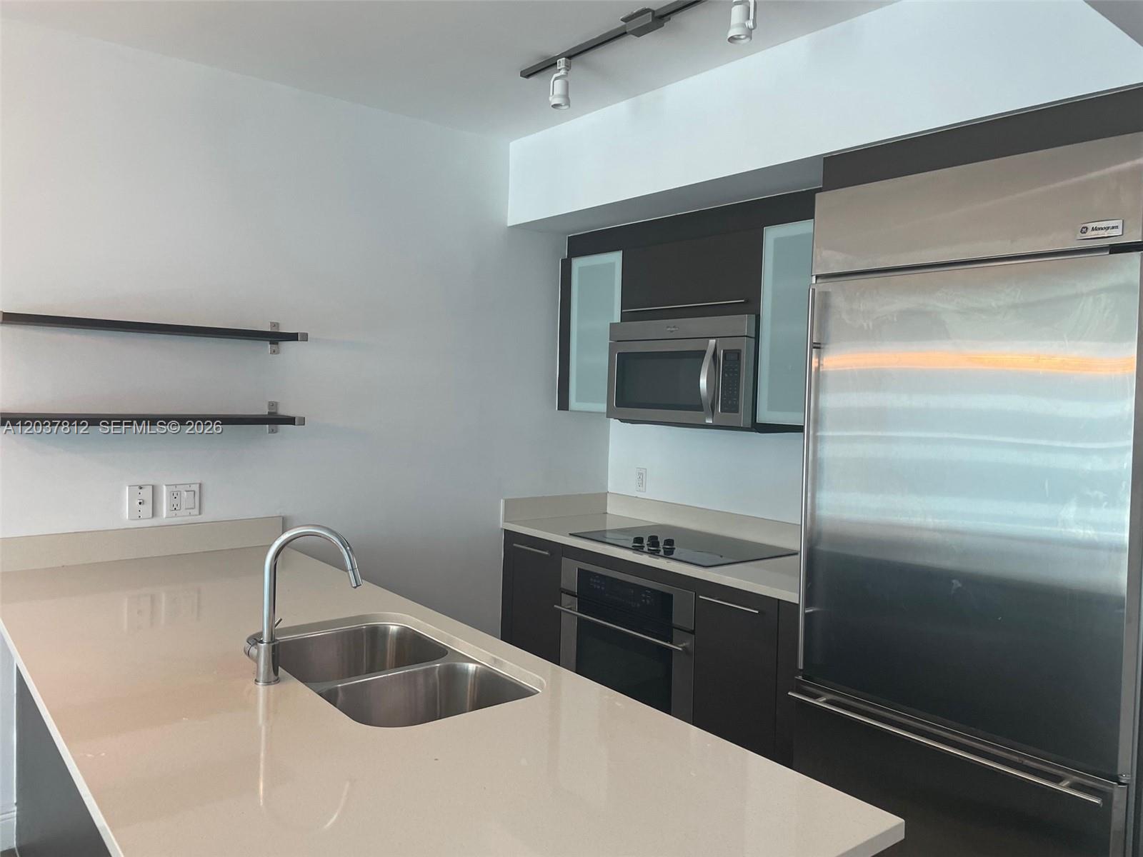 A modern kitchen features dark cabinetry, stainless steel appliances, and a light-colored quartz island countertop — 500 Brickell Av # 1906, Miami FL 33131, MIAMI, FL