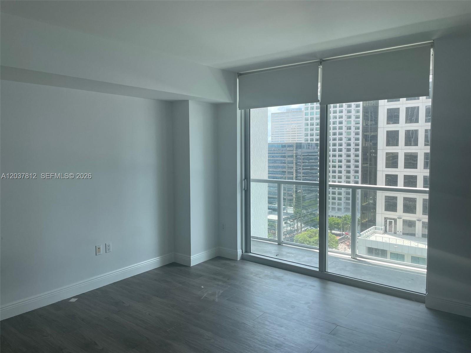 An empty room features gray wood-look flooring, white walls, and a balcony with city views — 500 Brickell Av # 1906, Miami FL 33131, MIAMI, FL