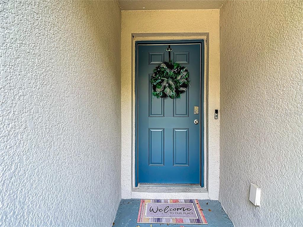 A blue front door with a wreath and a welcome mat sits in a recessed entryway — 5274 DIANTHA WAY, BROOKSVILLE, FL