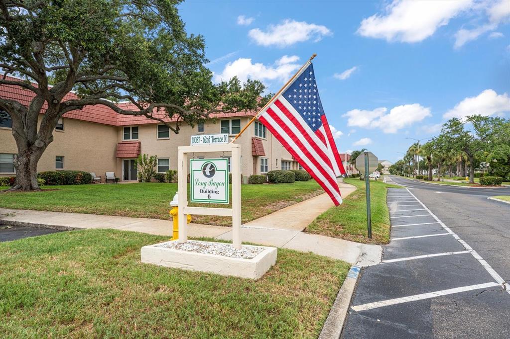 A tan apartment building with a red tile roof stands behind a Long Bayou sign — 10037 62ND TERRACE N UNIT 1, ST PETERSBURG, FL