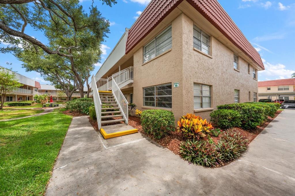 An exterior view of a two-story apartment building with a staircase and landscaped grounds — 10037 62ND TERRACE N UNIT 1, ST PETERSBURG, FL