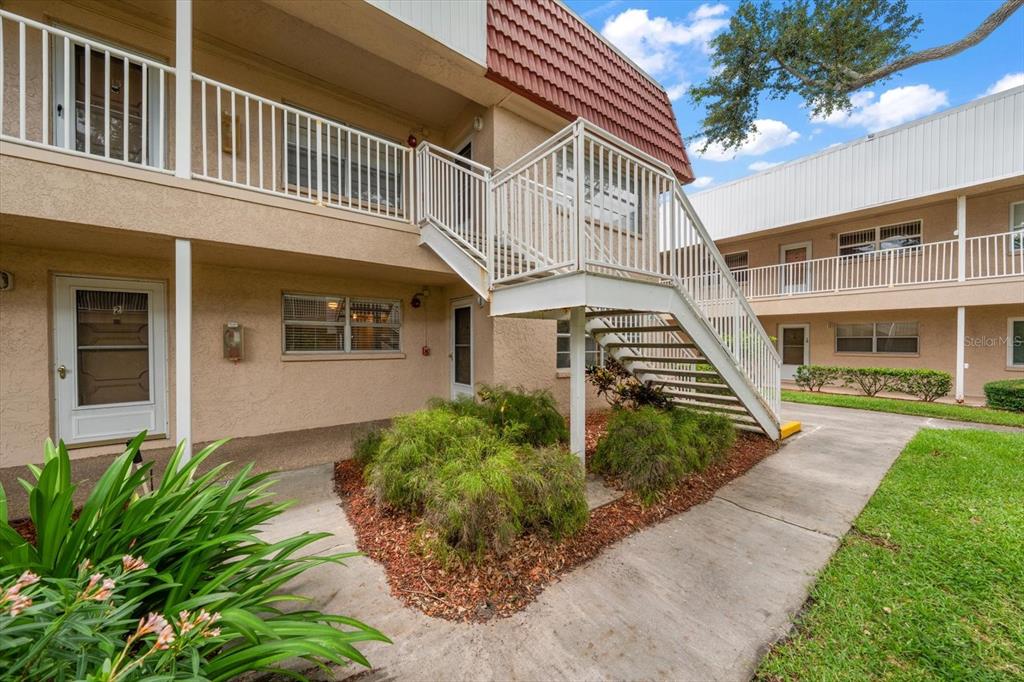 An exterior view of a two-story apartment building with a white metal staircase — 10037 62ND TERRACE N UNIT 1, ST PETERSBURG, FL