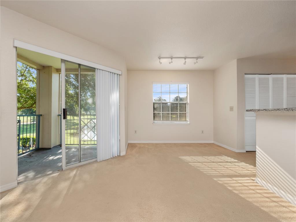 An empty carpeted living area features a sliding glass door to a balcony and a window — 7210 WESTPOINTE BOULEVARD UNIT 1325, ORLANDO, FL