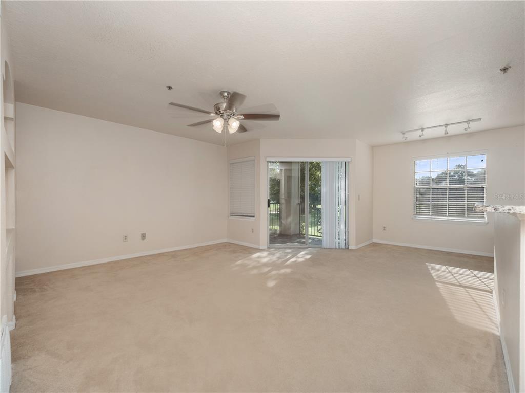 A carpeted living room features a ceiling fan, sliding glass doors, and a window — 7210 WESTPOINTE BOULEVARD UNIT 1325, ORLANDO, FL