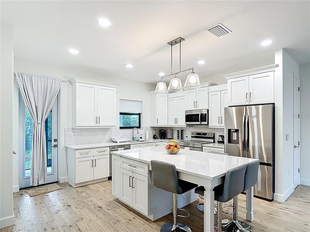 A modern kitchen features white cabinetry, a central island with bar stools, and stainless appliances — 12033 SARTO LANE, NORTH PORT, FL