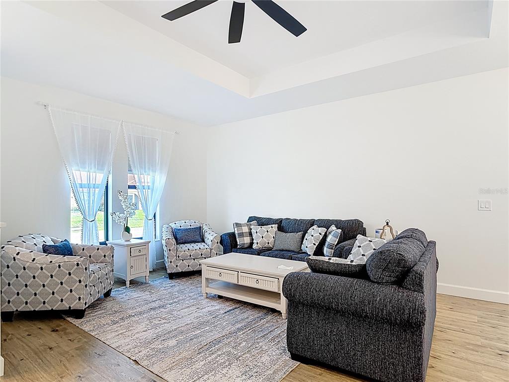 A living room features a dark sofa, patterned armchairs, a coffee table, and a ceiling fan — 12033 SARTO LANE, NORTH PORT, FL