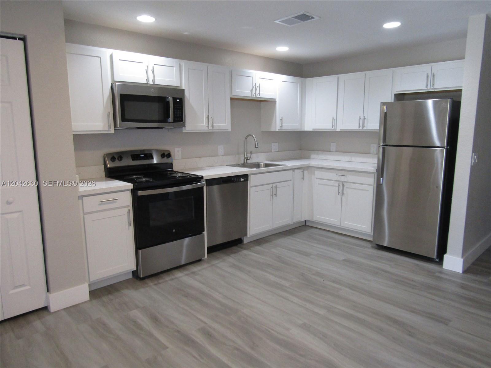 A kitchen features white cabinets, stainless steel appliances, and light wood-look flooring — 2703 S Ansel # 2703, Lehigh Acres FL 33973, LEHIGH ACRES, FL