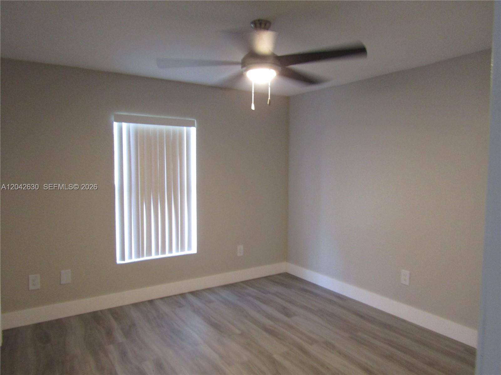 An empty bedroom features light gray walls, wood-look flooring, a ceiling fan, and a window — 2703 S Ansel # 2703, Lehigh Acres FL 33973, LEHIGH ACRES, FL