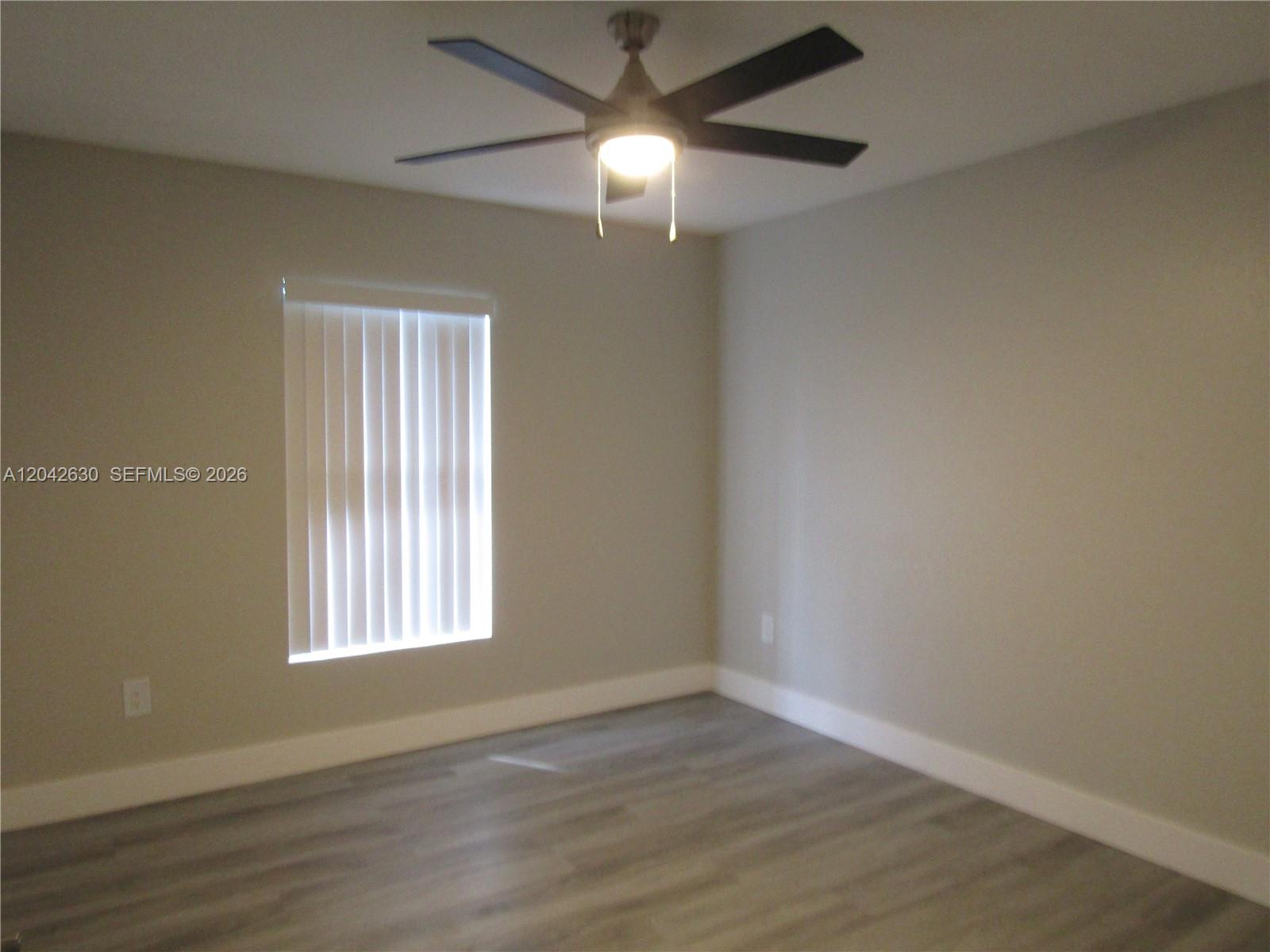 An empty bedroom features light gray walls, wood-look flooring, a ceiling fan, and vertical blinds — 2703 S Ansel # 2703, Lehigh Acres FL 33973, LEHIGH ACRES, FL