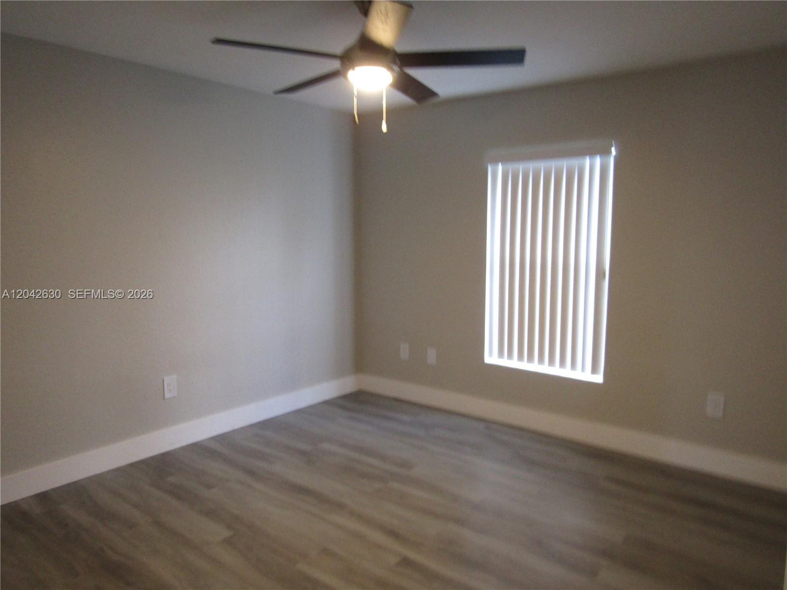 An empty bedroom features light gray walls, wood-look flooring, a ceiling fan, and a window — 2703 S Ansel # 2703, Lehigh Acres FL 33973, LEHIGH ACRES, FL