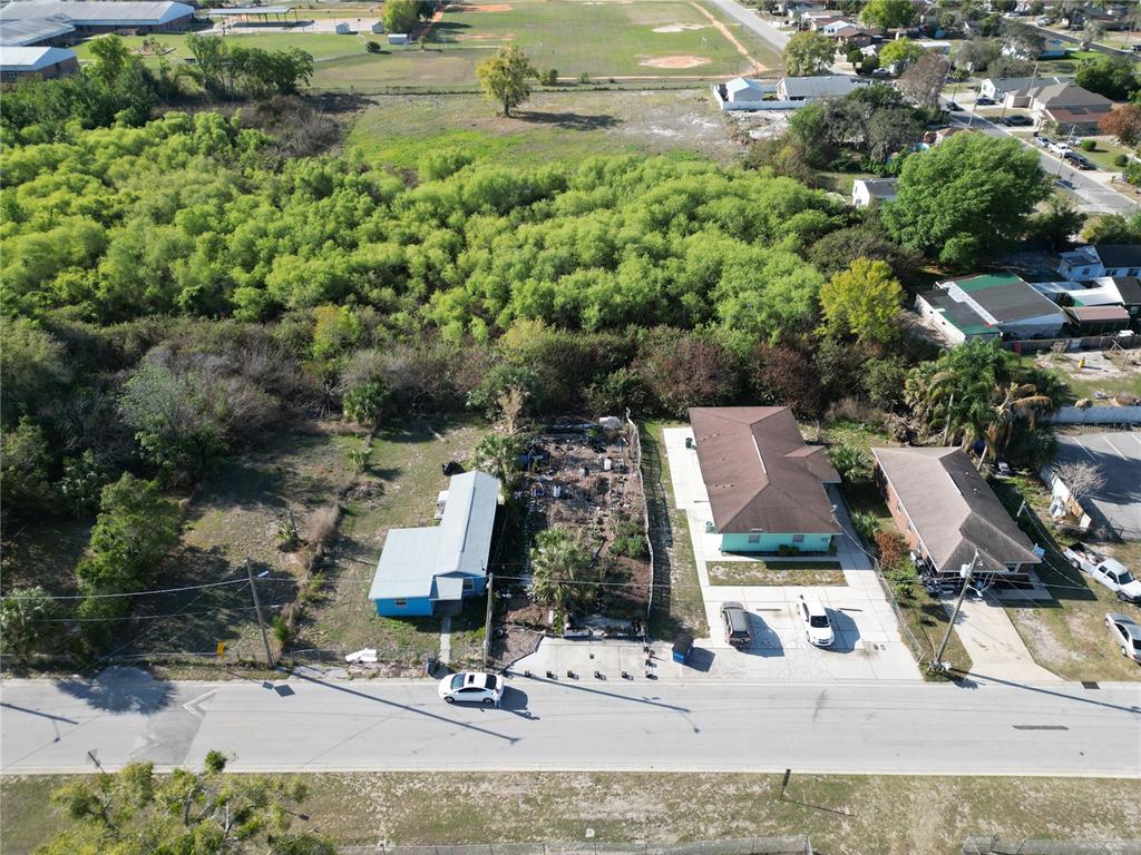 An aerial view shows three residential properties along a road bordering a large wooded area — 716 AVENUE Y NE, WINTER HAVEN, FL