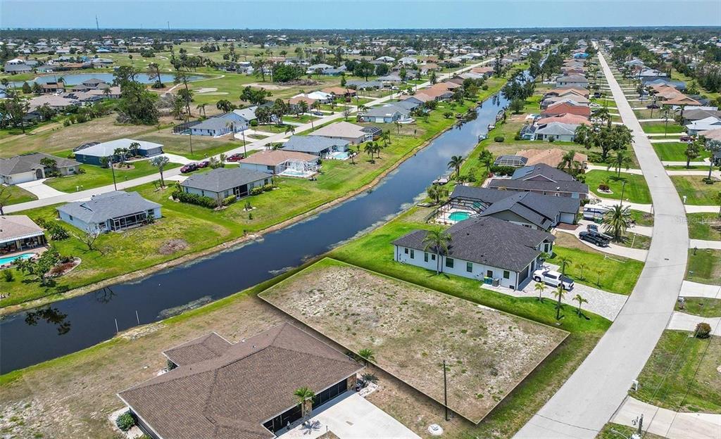 An aerial view shows a vacant residential lot situated between two houses along a canal — 168 MARK TWAIN LANE, ROTONDA WEST, FL