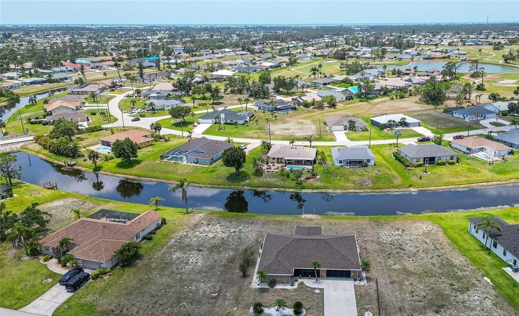 An aerial view shows a suburban neighborhood with houses, a canal, and vacant lots — 168 MARK TWAIN LANE, ROTONDA WEST, FL