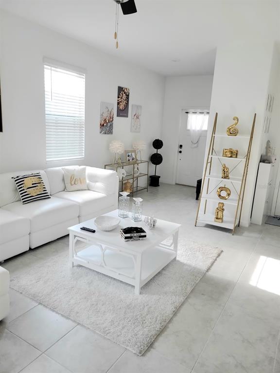 A bright living room features a white sofa, coffee table, and a gold-accented ladder shelf — 5131 FORUM BOULEVARD, HOLIDAY, FL