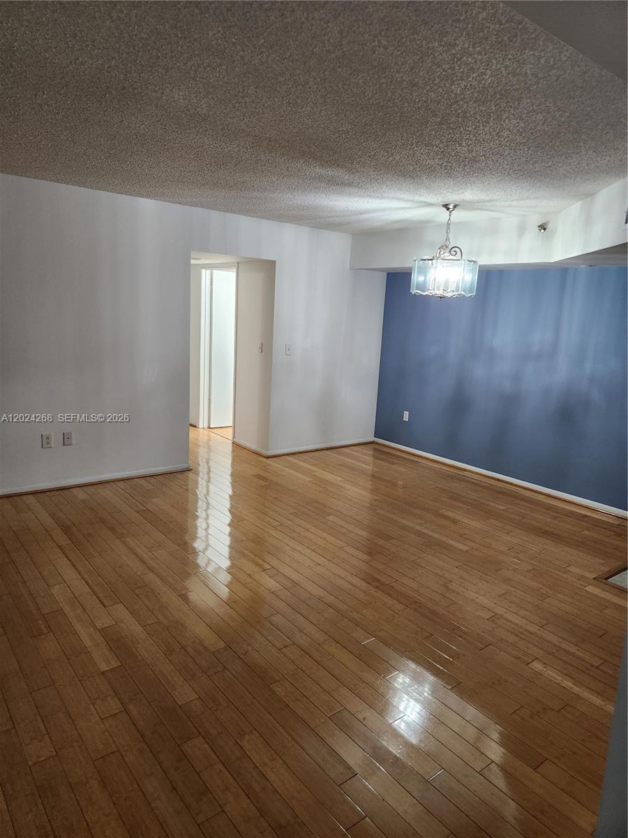 An empty room features hardwood flooring, white walls, a blue accent wall, and a chandelier — 5900 Collins Ave # 404, Miami Beach FL 33140, MIAMI BEACH, FL