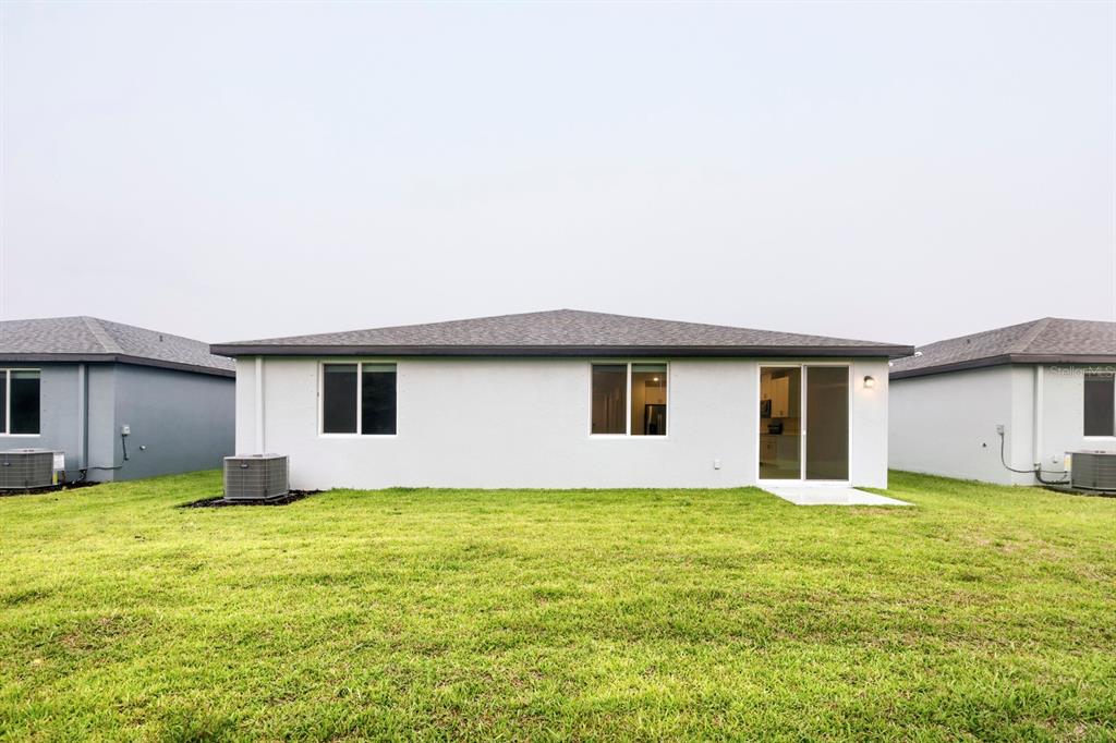 The back exterior of a single-story house features a white stucco wall, windows, and sliding doors — 7637 SATTERFIELD TERRACE, PARRISH, FL