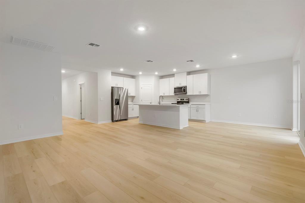 A bright, open-concept kitchen features white cabinetry, stainless steel appliances, and light wood flooring — 7637 SATTERFIELD TERRACE, PARRISH, FL