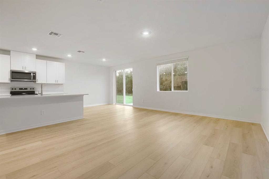 An open-concept kitchen and living area features white cabinetry, light wood flooring, and sliding doors — 7637 SATTERFIELD TERRACE, PARRISH, FL