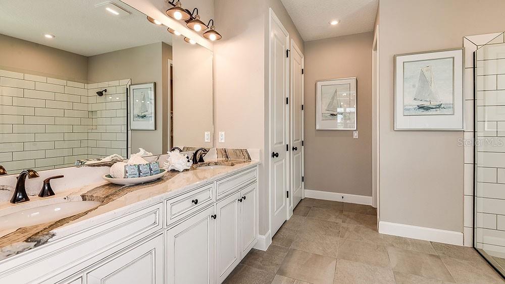 A bathroom features a double vanity with stone countertops, white cabinetry, and a tiled shower — 6933 PRAIRIE OAK WAY, NOKOMIS, FL